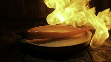 Red hot chili pepper on black background with flame, spicy food concept. Stock footage. Close up of a pepper lying on a wooden board under the hot flame. photo