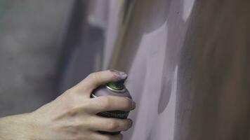 A hand with a spray can that draws a new graffiti on the wall. Photo of the process of drawing a graffiti on a wooden wall close-up. The concept of street art and illegal vandalism