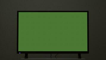 Plasma TV with green screen stands on background wall. Concept. Green-screen TV stands on background gray wall. Green screen TV for inserting chromakey photo