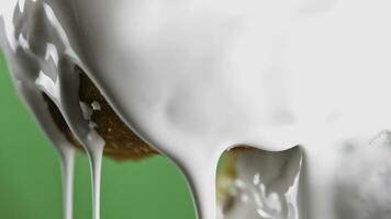 Donut with dripping white icing. Stock clip. Close-up baking with stream of white cream. White cream drips from bun on green background. Baking and cooking photo