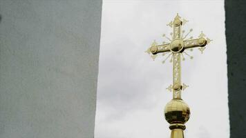 Religion and faith concept, bottom view of a golden cross of the church. Video. Big golden cross on cloudy sky background. photo