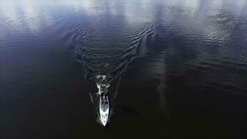 Top view of a man practising on a surfboard with a rowing paddle in the lake, sport and lifestyle concept. Footage. Aerial of a man standing on a surfboard and rowing in calm water. photo