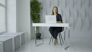mujer en traje trabajando en un moderno oficina a el mesa. acción. blanco paredes, verde planta y un mesa con un computadora portátil, minimalista estilo. foto