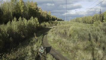 Top view of ATVs driving on off-road. Clip. Pair of military ATVs rides off-road in wooded area. ATVs ride on field road near autumn forest on sunny day photo