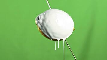 Modern art concept. Stock clip. Close up of lemon fruit on a wooden skewer being poured by white liquid paint isolated on a green wall background. photo