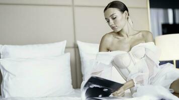 A young well-groomed model in a white dress on the bed. Action. A woman carefully leafing through a magazine lying in a bright spacious room. photo