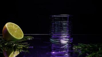 Close up of transparent glass standing on a bar counter with green decorative plant and orange fruit. Stock clip. Dark purple background at the night club. photo