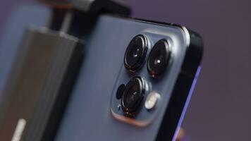 Russia - Moscow, 09.28.2021. extreme close up of cameras of a new Iphone 13 pro max fixed by steadicam. Action. New smartphone isolated on purple wall background. photo