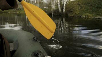 Close up of a man on a river in a green rubber boat with a yellow paddle. Stock footage. Male rowing with an oar sitting in a rubber boat. photo