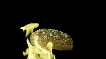 An appetizing burger bun with sesame seeds isolated on black background with red flame. Stock footage. Food and cooking concepr, rotating baked bun in flame. photo