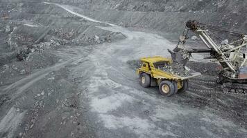 Top view of excavator in open pit. Excavator falls asleep rubble in dumper on outdoor quarry in extraction of minerals. Concept of extraction of minerals photo