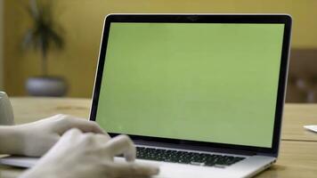 Close-up of freelancer sitting at laptop with green screen. Stock footage. Man is typing on laptop with green screen working in freelance and cozy atmosphere photo