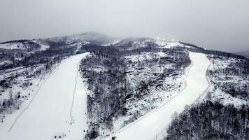 Top view of ski resort in cloudy weather. Stock footage. Beautiful snowy mountains with forests and ski trails on background of fog and overcast winter sky photo