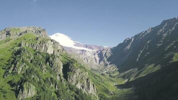 parte superior ver de montaña verde paisaje con rocas y Nevado pico en antecedentes de azul cielo. acortar. montaña garganta con verde arboles y agudo rocas mira espectacular. verano montaña paisaje foto