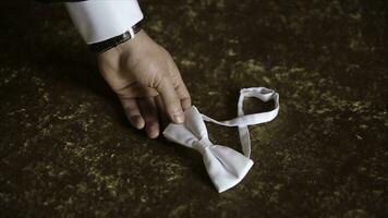 Groom's hand takes a bow tie. Preparing to wedding day. The man takes the bow-tie. Wedding accessories. Groom holding brown bow tie in his hand. Man holding bow tie. Elegant gentleman clother. Wedding photo