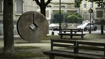 Modern city park with benches and metal round statue with a diamond-shaped hole in the middle of it. Stock footage. A public place with trees near the road. photo