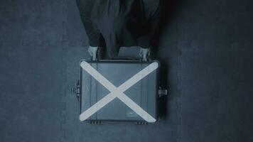Top view of a hacker man wearing hood opening silver suitcase with a white cross. Stock footage. Mysterious case that lying on concrete surface being opened by a man. photo