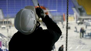 Preparation of stadium with workers. Stock footage. Man in hard hat speaks on radio with workers preparing stadium for competition photo