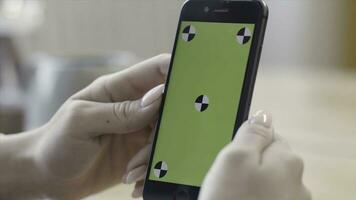 Close up of woman hands holding smartphone with green screen display in verical position. Stock footage. Female looking at her device with chroma key and traking marks. photo