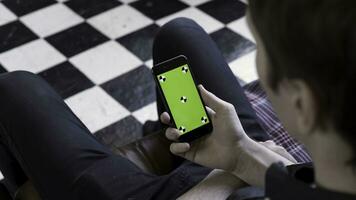 Male holding black smart phone with green screen and tracking marks on black and white checkered floor background. Stock footage. Man using and watching at mobile phone with chroma key. photo