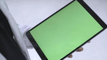 Close-up view of man in white doctor's coat and black shirt tapping on the tablet with chroma key green screen. Stock footage. New technology concept photo