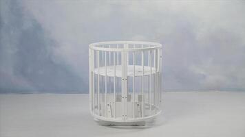 Baby white cradle swinging in the empty room in front of a wall coloured in light blue. Stock. White small baby bed swinging from one side to another in light empty room. photo