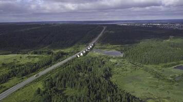 Top view of bridge passing through in forest. Clip. Highway passes through swamp in forest to city on horizon. Traffic on rural highway in cloudy weather photo