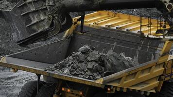 Excavator fills dump truck. Bucket excavator closeup loads stones into body of dump truck on mining or construction of something photo