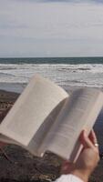 book in hands on the background of the ocean and waves. Vertical video