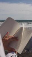 book in hands on the background of the ocean and waves. Vertical video