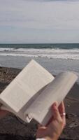 bok i händer på de bakgrund av de hav och vågor. vertikal video