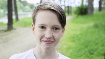 de cerca de linda adolescente sonriente en verano. concepto. chico sonrisas dulcemente y mira a cámara en antecedentes de bosque. linda y hermoso chico sonrisas mirando a cámara en verano bosque foto