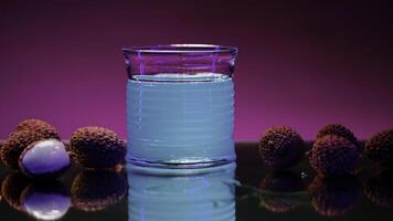 Refreshing non alcoholic beverage of blue color isolated on pink lighted wall background. Stock clip. Bar counter decorated by lychee berries. photo