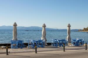 Open air Cafe on the seashore with blue chairs and folded umbrellas in Aegina, Greece photo