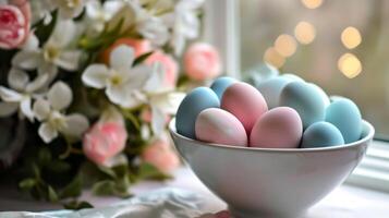 ai generado un blanco cuenco lleno con azul y rosado huevos sentado en parte superior de un mesa siguiente a un manojo de flores foto