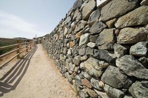 un imagen a lo largo un excursionismo ruta con un Roca pared y un de madera cerca foto
