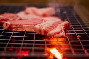 Grilling pork on stainless steel grill with flames on black background, food and cuisine concept. Burning pork on a charcoal grill. photo