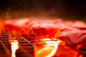 Grilling pork on stainless steel grill with flames on black background, food and cuisine concept. Burning pork on a charcoal grill. photo