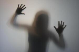 Woman Silhouette with Raised Hands Behind Frosted Glass photo