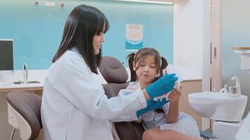 dentista feminina demonstrando como escovar os dentes para uma garotinha na clínica odontológica, check-up de dentes e conceito de dentes saudáveis video