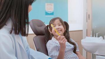 femme dentiste démontrant comment se brosser les dents à une petite fille dans une clinique dentaire, un examen des dents et un concept de dents saines video