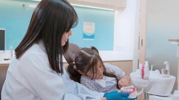 Female dentist demonstrating how to brush teeth to a little girl in dental clinic, teeth check-up and Healthy teeth concept video