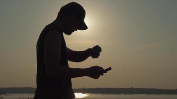 joven hombre cheques el hora en su rutina de ejercicio reloj antes de trotar para un sano rutina de ejercicio cerca puesta de sol. video