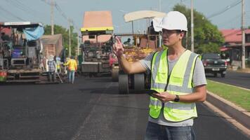 Asian engineers watch road rebuilding workers and asphalt machines of the road at the construction site. video