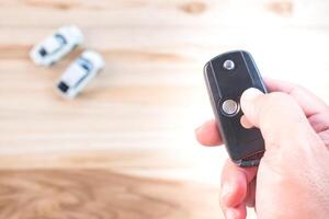 Asia a man push remote control of car key for lock and unlock system toy car model concept on wood table photo