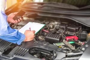 Hand mechanic hold check sheet paper and smart phone for basic checking a engine of car,maintenance and service check in garage photo