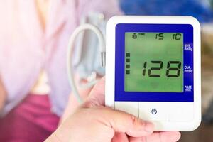 Close up blood pressure monitor in hand a man and heart digital gauge with elderly people for basic health check in home photo