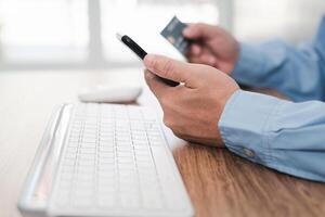 Hand a man hold smartphone credit card and computer desktop keyboard and mouse on table for working and pay money in shopping on line photo