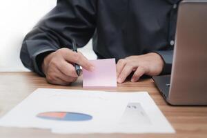 Business man use paper note memo job details laptop computer calculate and analyzing with document data graph for new project of business strategy at workplace photo