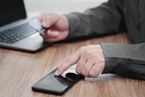 Businessman use smartphone make online banking, making a payment or purchasing on the internet entering his credit card details and use laptop working on table photo